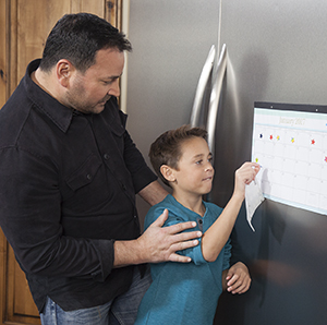 Man watching boy put sticker on calendar page.