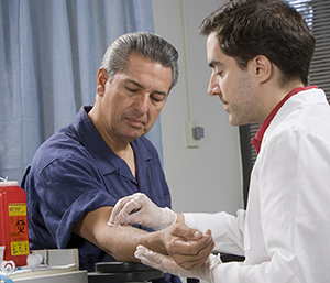 Health care provider taking blood from man's arm.