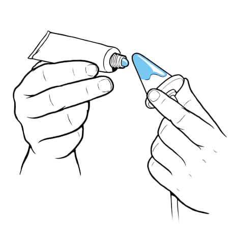 One hand holding open lubricant tube toward cone and other hand holding tip of cone at end of tubing.