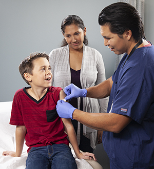 Health care provider covering injection site on boy's arm with a Band-aid.