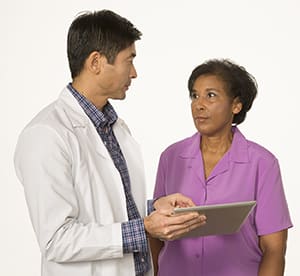 Doctor holding tablet, talking to woman.
