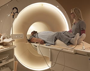 Person lying on table of MRI machine, preparing for MRI with help of technician.